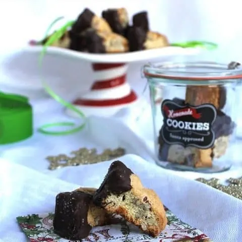 Dark Chocolate Salted Caramel Almond Biscotti on a festive napkin, in a container and on a server platter