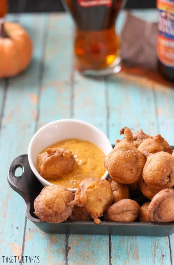 Overhead of andouille sausage corn dog bites and a small bowl of mustard in a black serving dish