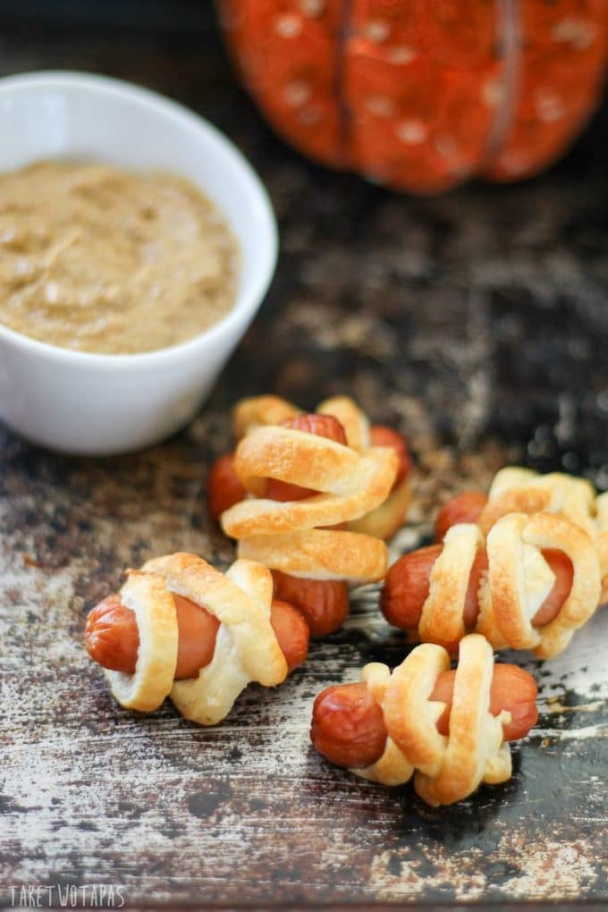 Mummy Pups and a small white bowl of devilish mustard on a sheet pan