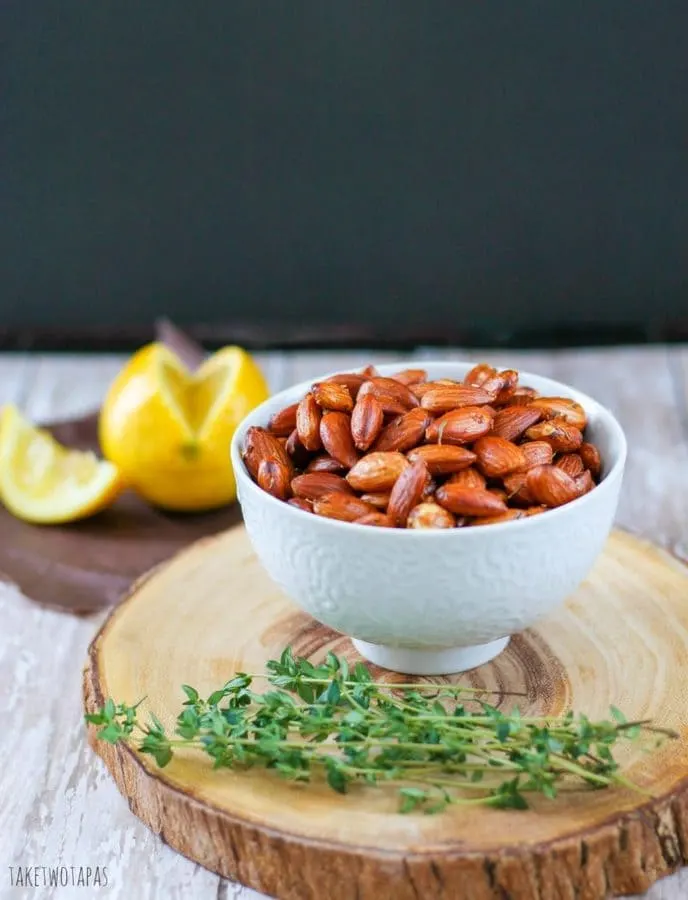 Toasted Lemon Thyme almonds in a white bowl sitting on a wood platter