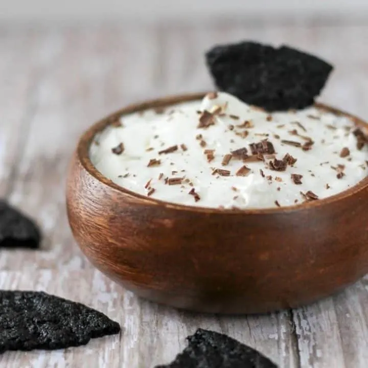 Side view of oreo cheesecake dip in a wood bowl with a chocolate wafer sticking out of it.