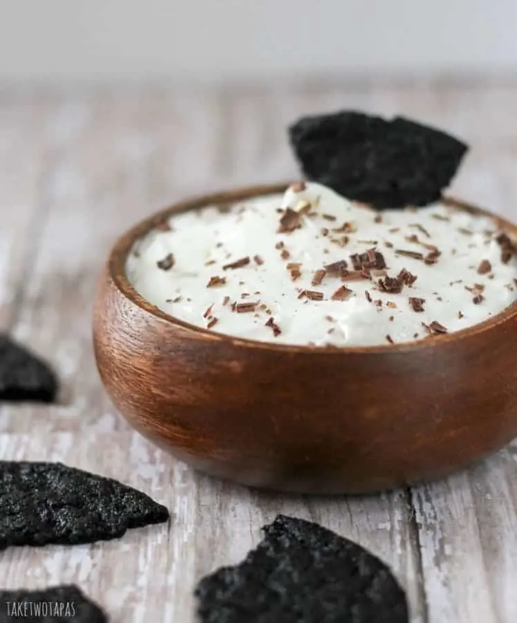 Side view of oreo cheesecake dip in a wood bowl with a chocolate wafer sticking out of it.
