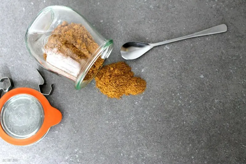 overhead of spicy Chai Spice Mix spilling out of a glass jar on to a table with a spoon next to it.