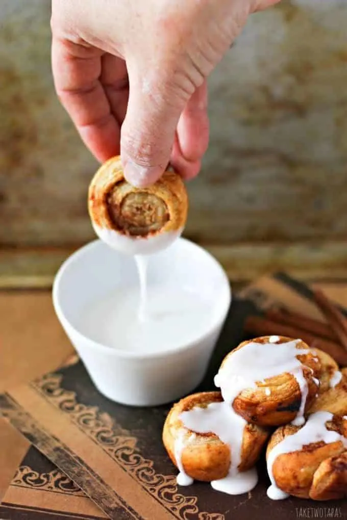 Hand dipping a cinnamon roll in to a small white bowl of icing