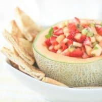 Salsa in a cantalope with chips in a white bowl