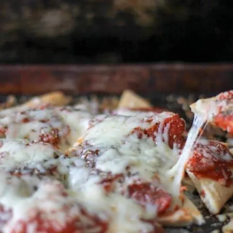 close up of a pizza nacho being take from the sheet pan
