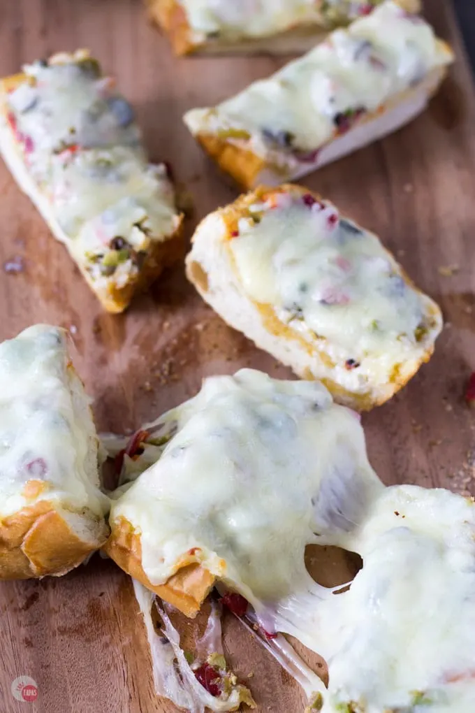 Overhead of cut cheesy olive bread with olive salad on a wood surface.