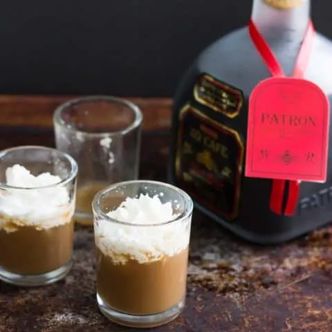 White russian shots and a bottle of Patron on a dark surface