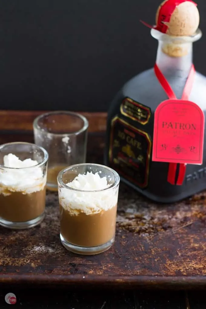White russian shots and a bottle of Patron on a dark surface