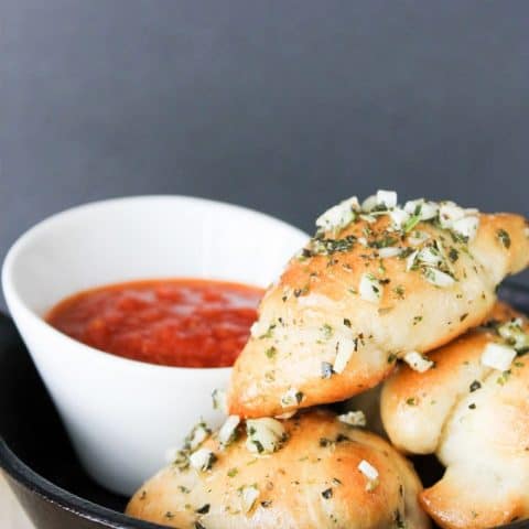 5 ingredient garlic knots and a small white bowl of tomato sauce in a black platter
