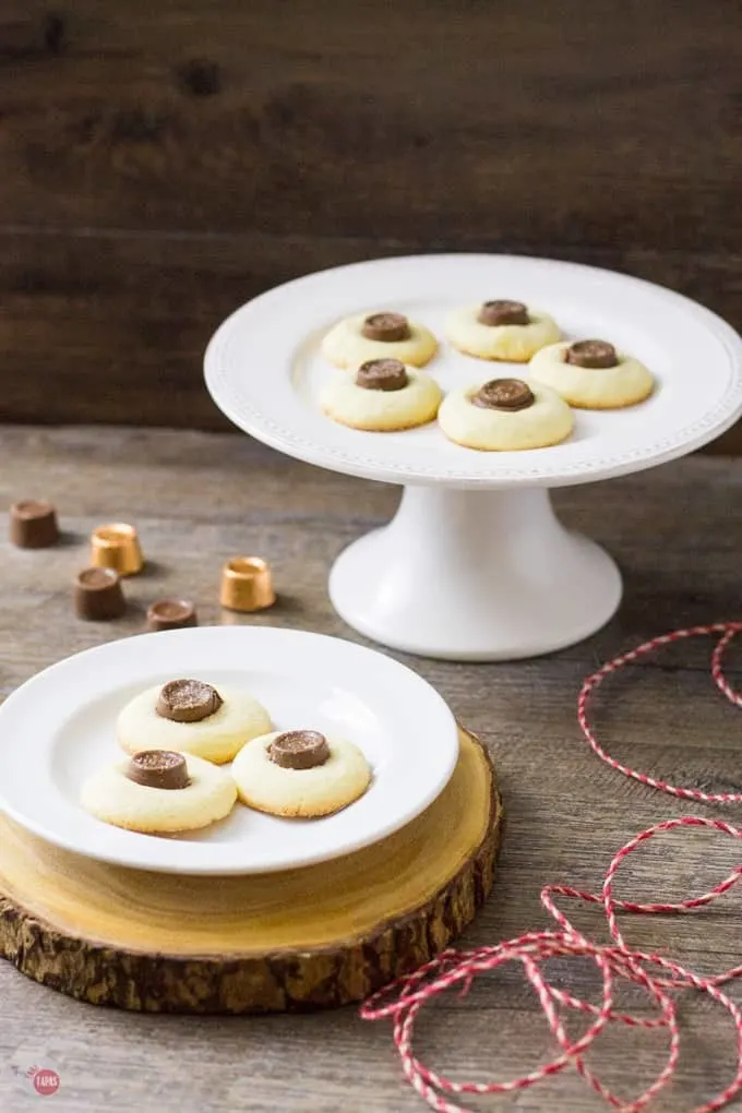 Salted rolo thumbprrint cookies on a white latter and on a white plate both on a wood surface.