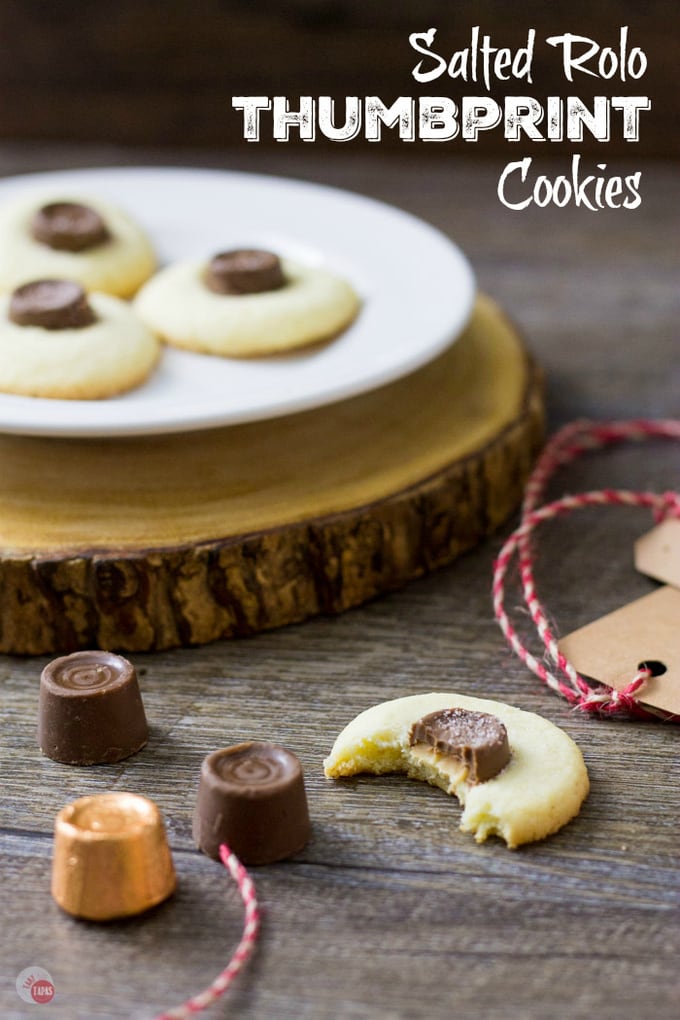 thumbprint cookies on a white plate, rolos, and a half eaten cookie on a wood surface and text "salted rolo thumbprint cookies"