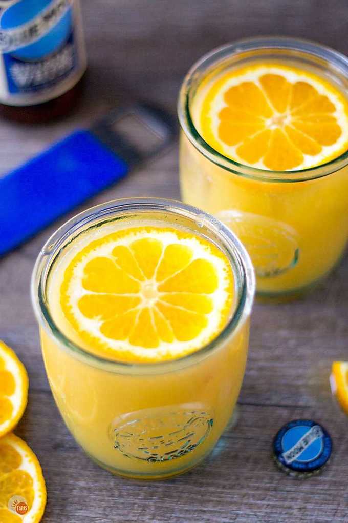 Two Satsuma Orange Shandy cocktails with an orange slice floating on top.