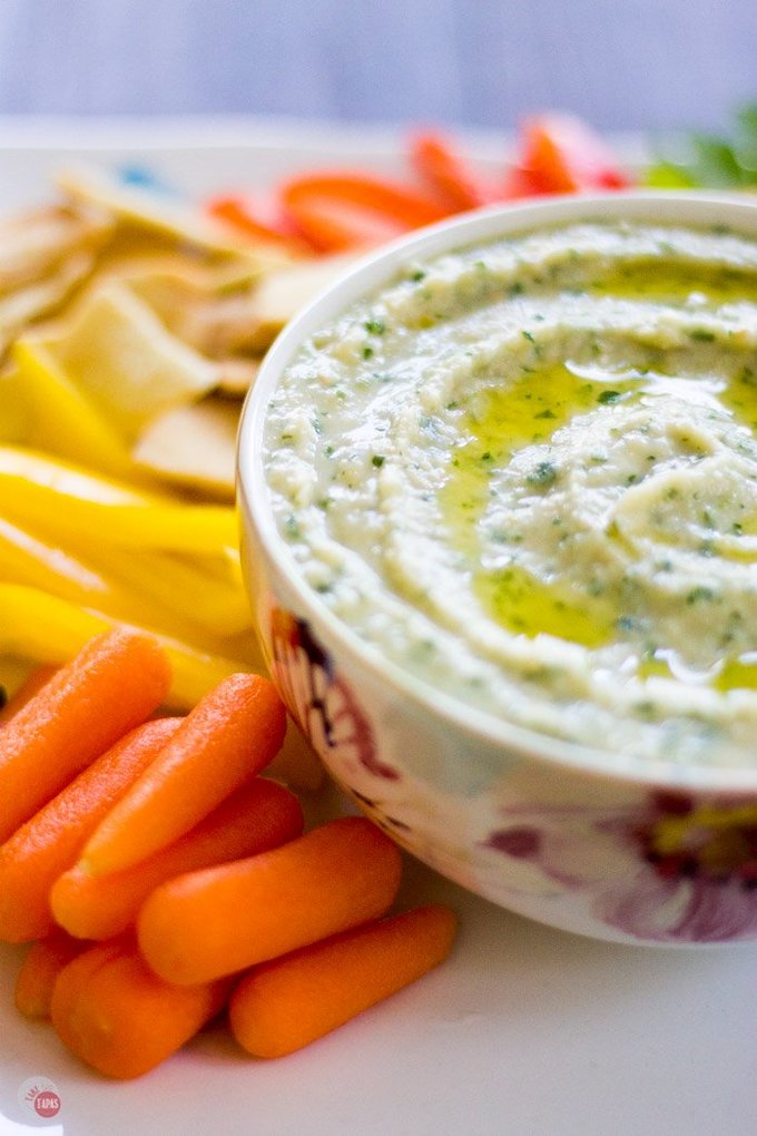 Side view of hummus in a flowered bowl and carrots on a white platter.