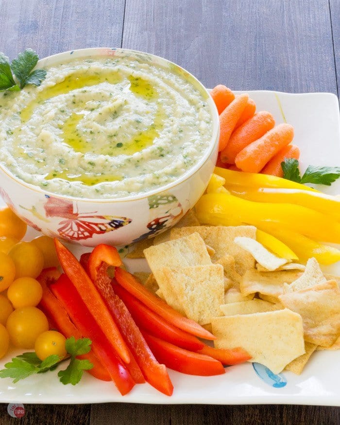 White Bean Parsley hummus in a white bowl and assorted vegetables and chips on a white platter.