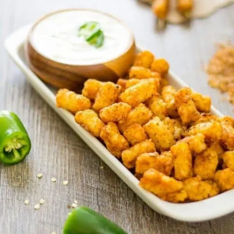 Steakhouse tater tots and jalapeno ranch dip in a wood bowl all on a white platter.