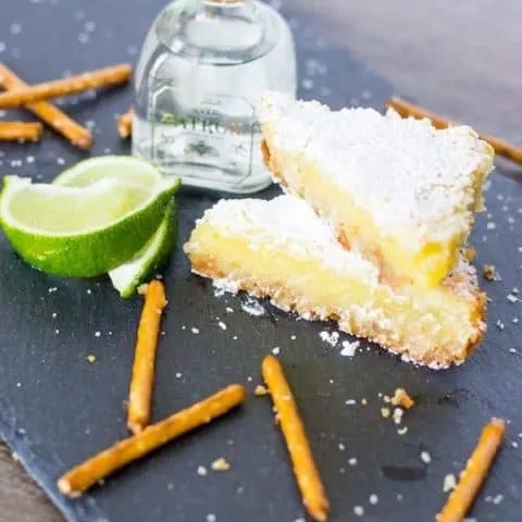 Margarita Bars stacked, pretzel sticks, lime wedges, a small bottle of tequila on a slate board