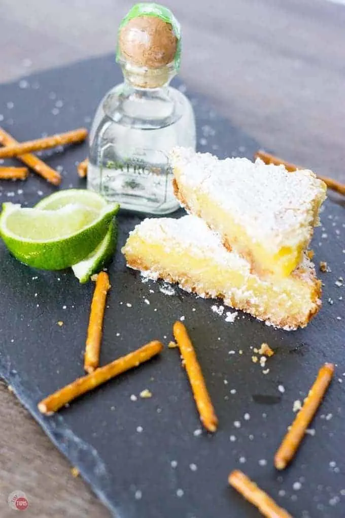 Margarita Bars stacked, pretzel sticks, lime wedges, a small bottle of tequila on a slate board