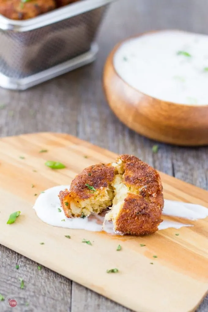 Southwest Potato Croquette with a bite out of it sitting on top of some green chile ranch sauce on a cutting board