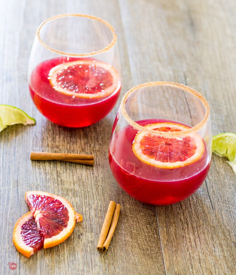 Blood Orange Cinnamon Margarita, blood orange slices, lime wedges and cinnamon sticks on a wood surface