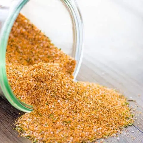 Dry Rub BBQ Seasoning Blend spilling out of a jar on to a wood surface