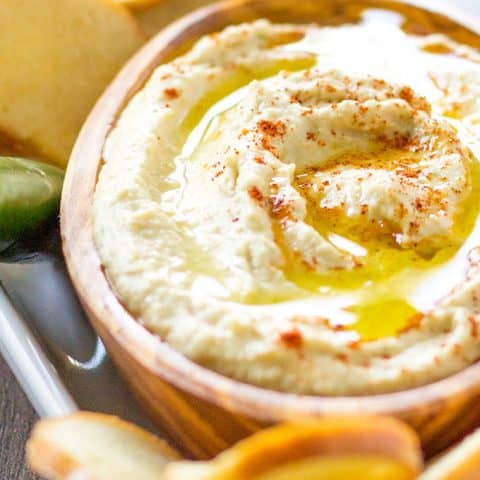 Smoky Pineapple Hummus with Serrano Pepper in a wood bowl surrounded by bagel chips on a white platter