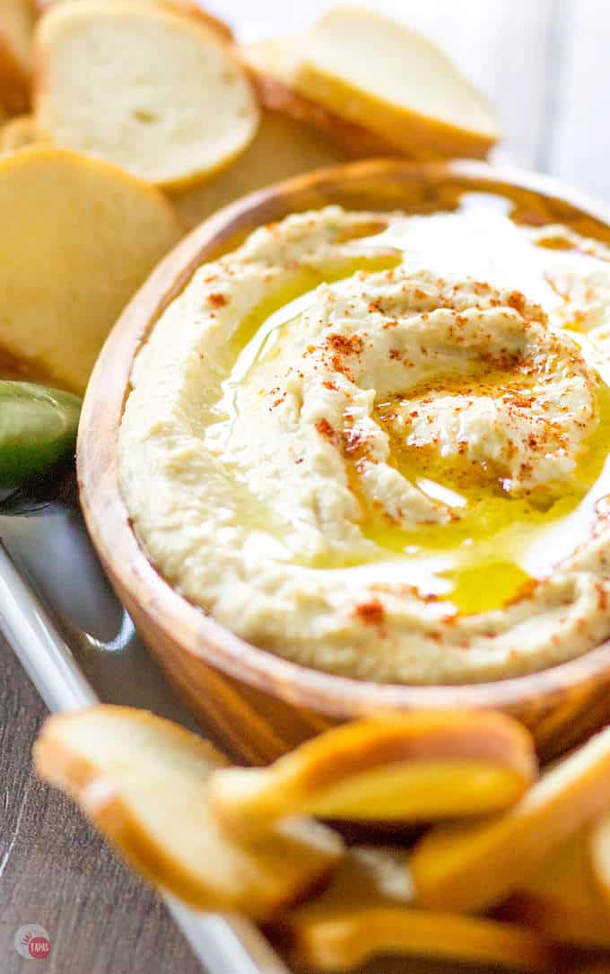 Smoky Pineapple Hummus with Serrano Pepper in a wood bowl surrounded by bagel chips on a white platter