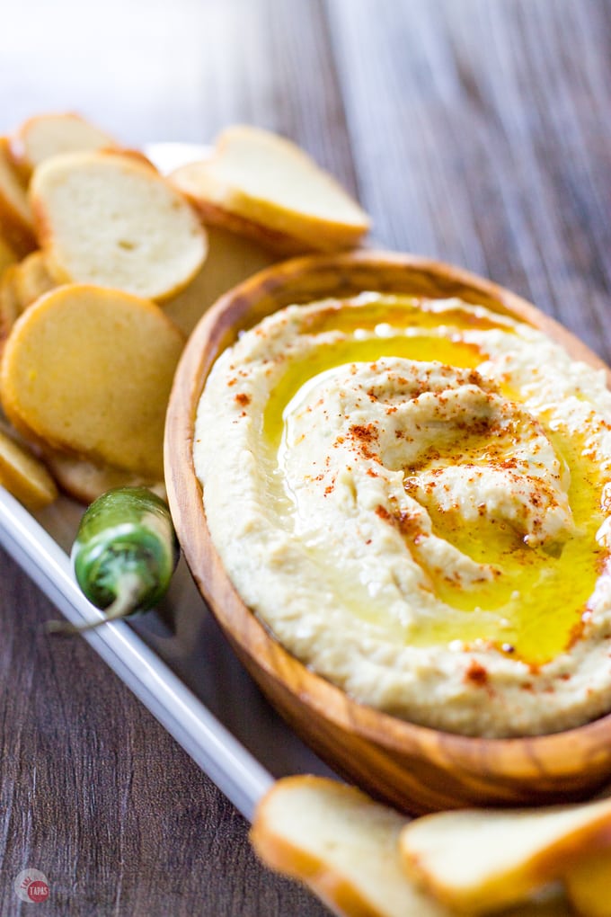 Close up of Pineapple Hummus with Smoked Paprika in a wood bowl on a platter with bagel chips and a serrano pepper