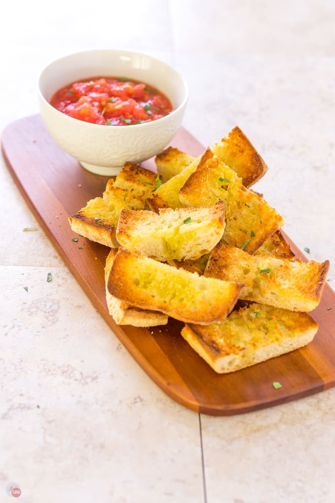 Pan Con Tomate in a small white bowl and pieces of spanish grilled toast on a wood platter