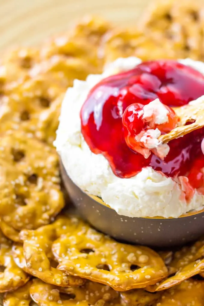 Close up of Pretzel chip dipped in the Cherry Pretzel salad dip in a dark gray bowl with pretzel chips around it.