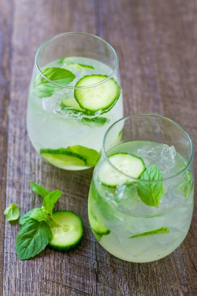 overhead of 2 cucumber mint gin cooler cocktails o a wood table.