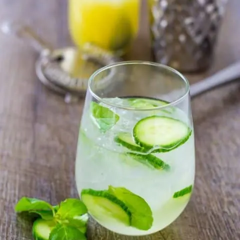 Herbaceous Cucumber Mint Gin Cooler with lime sparkling water on a wood table with tools to make it in the background.