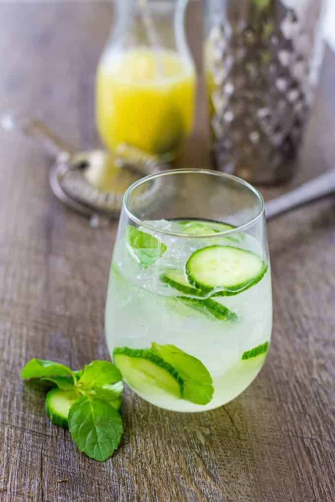 Herbaceous Cucumber Mint Gin Cooler with lime sparkling water on a wood table with tools to make it in the background.