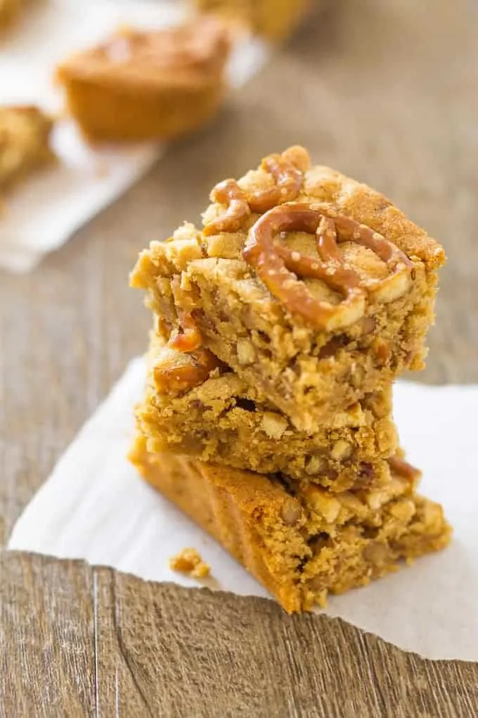Stacked Peanut Butter Pretzel Bars with Bourbon and Bacon on parchment paper on a wood surface
