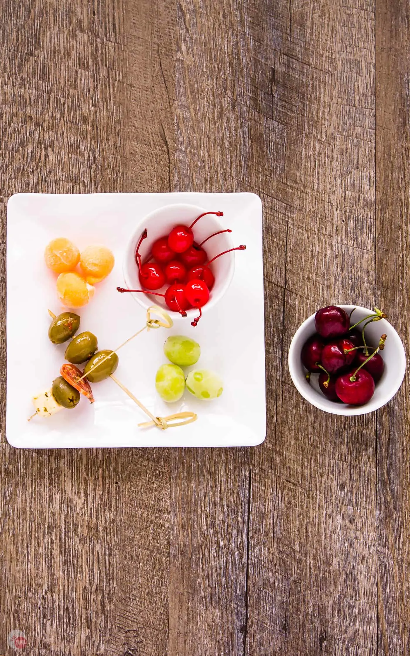 Skewered olives, 2 different cherries in bowls and sugared grapes on a plate