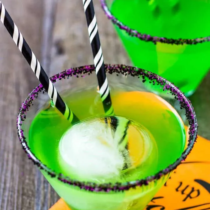 close up of green flying monkey halloween cocktail with 2 black striped straws in it