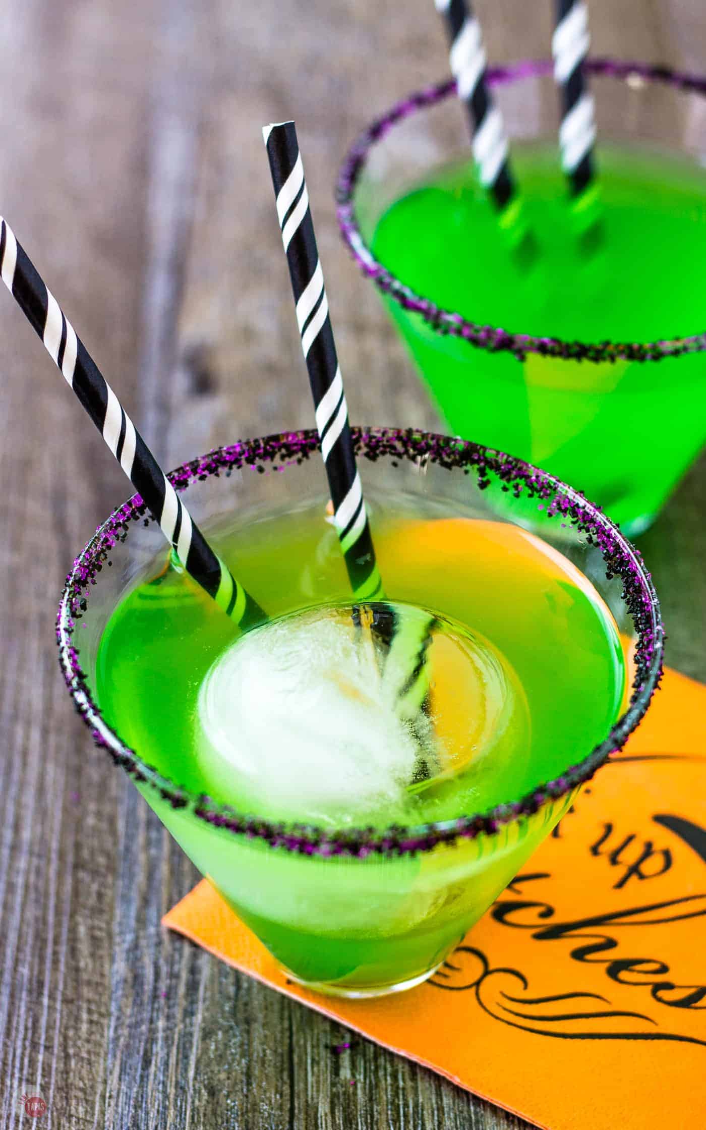 close up of green flying monkey halloween cocktail with 2 black striped straws in it