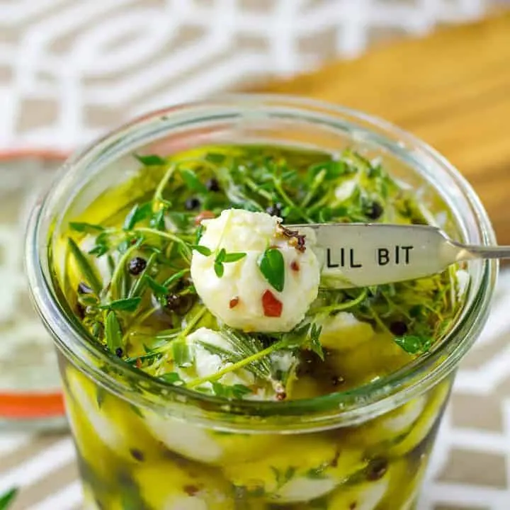 overhead of Herb Marinated Goat Cheese Balls in a glass jar sitting on a brown and white placemat