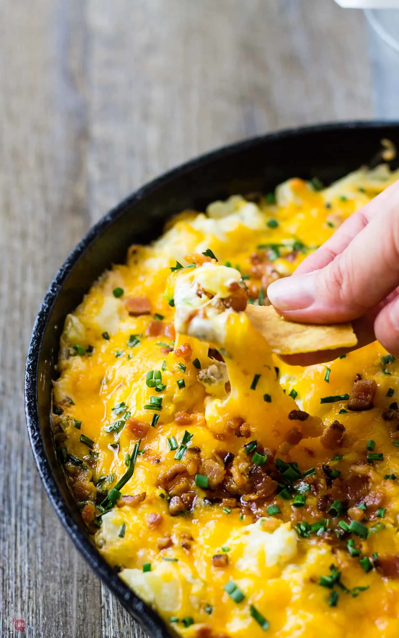 hand dipping chip into cast iron skillet filled with loaded potato skin dip
