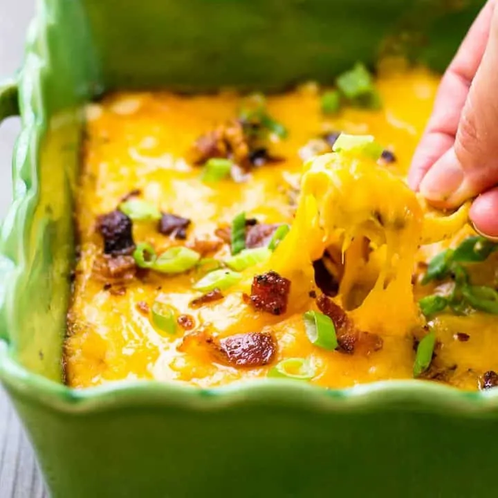 Chicken Bacon Ranch Crock Pot Dip in a green serving dish and a hand dipping a chip in it.