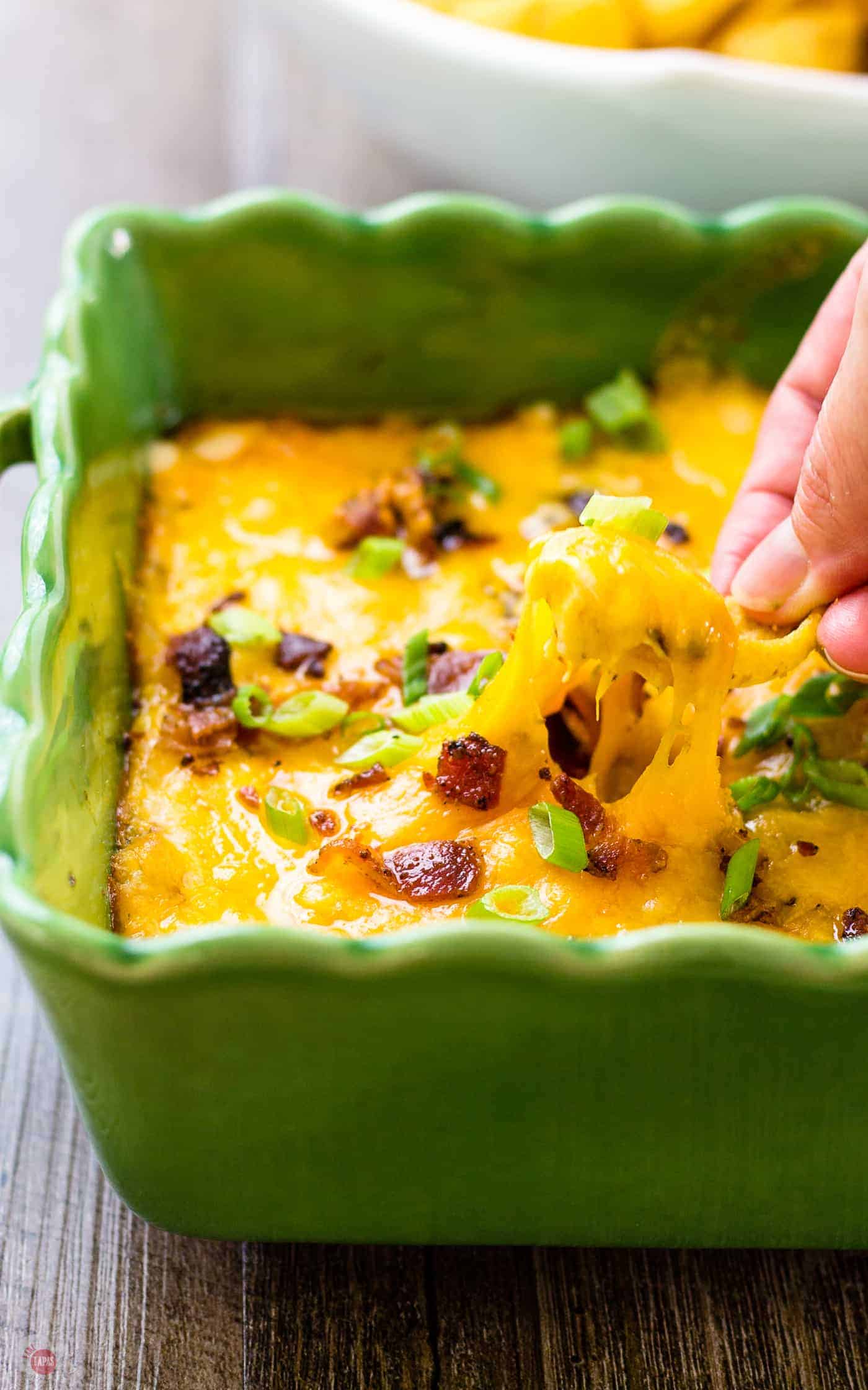 Chicken Bacon Ranch Crock Pot Dip in a green serving dish and a hand dipping a chip in it.