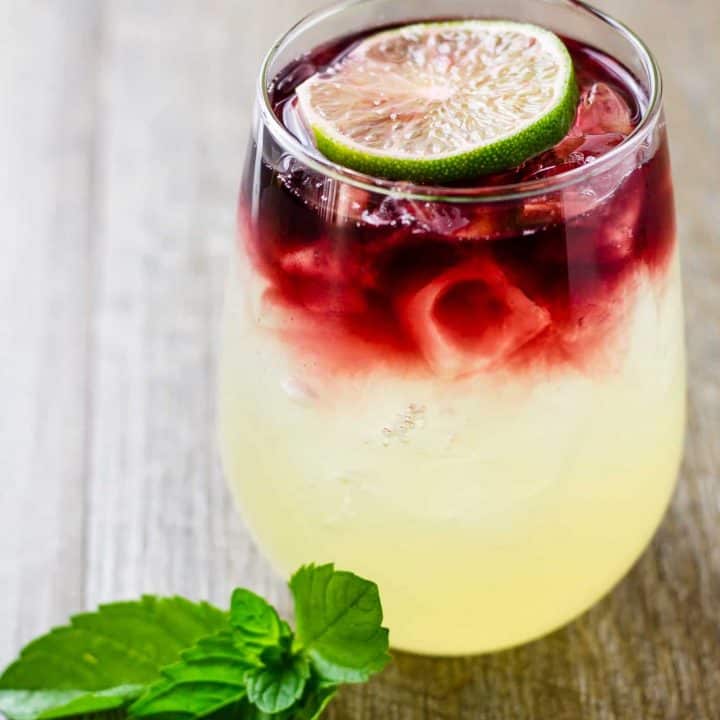 Side view showing the layers of limeade and wine in the glass sitting on a wood table.