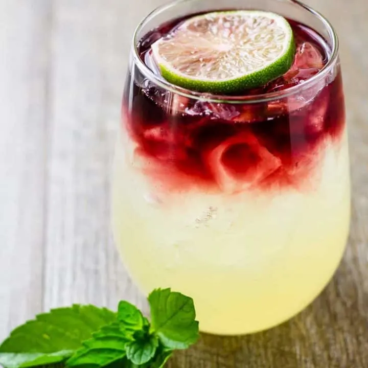 Side view showing the layers of limeade and wine in the glass sitting on a wood table.