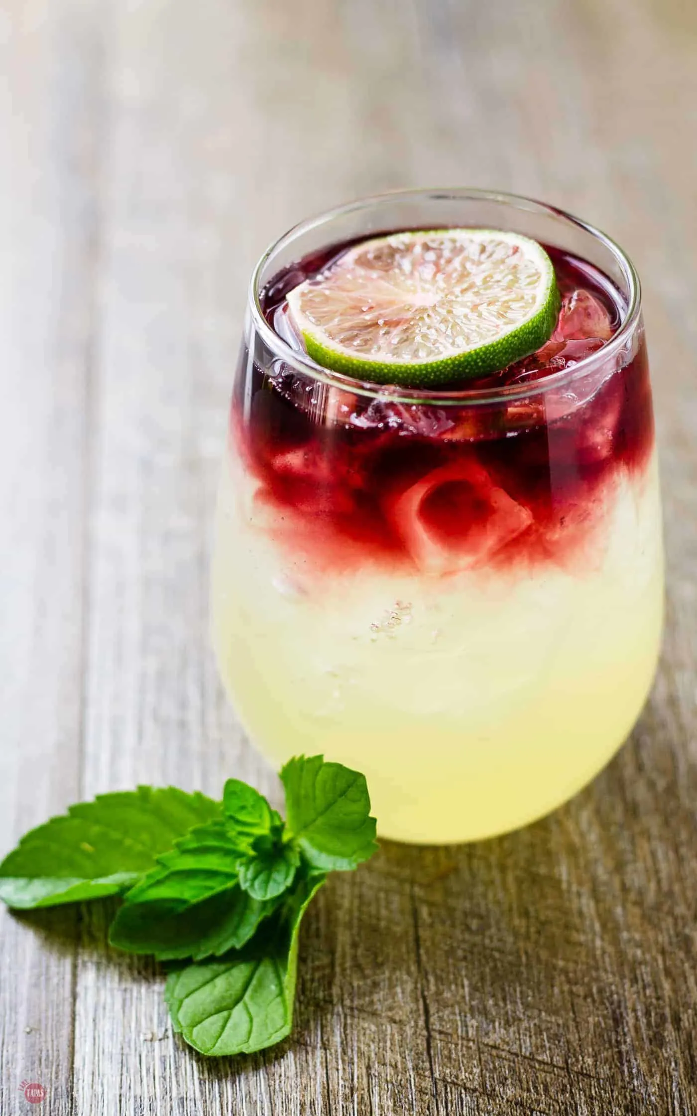 Side view showing the layers of limeade and wine in the glass sitting on a wood table.