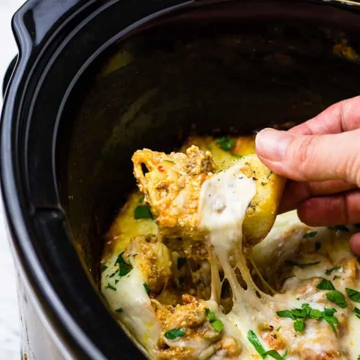 Hand dipping breadstick into the extra cheesy lasagna dip, in a crockpot!