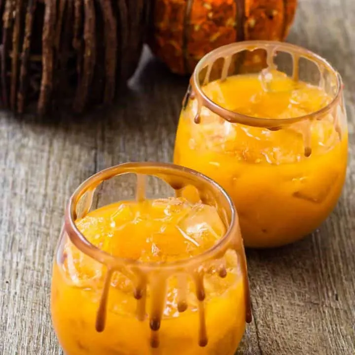 2 cocktails with the chocolate caramel sauce dripping on the glasses sitting on a table