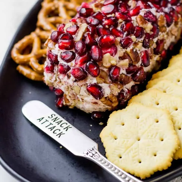 Close up of Pomegranate Drunken Goat Cheese Log, crackers and pretzels on a black platter.