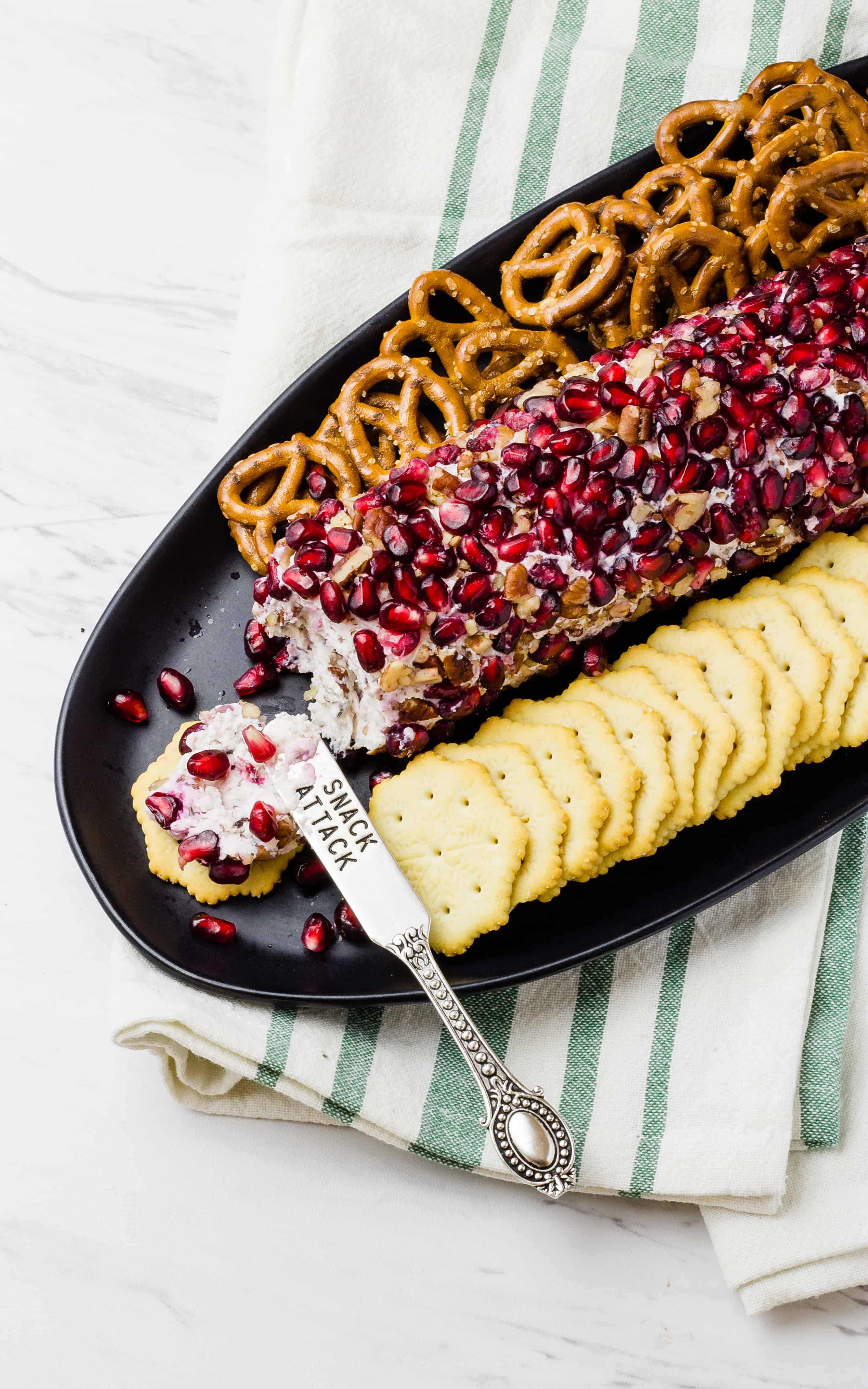 Overhead of drunken pomegranate goat cheese log, crackers and pretzels on a black platter