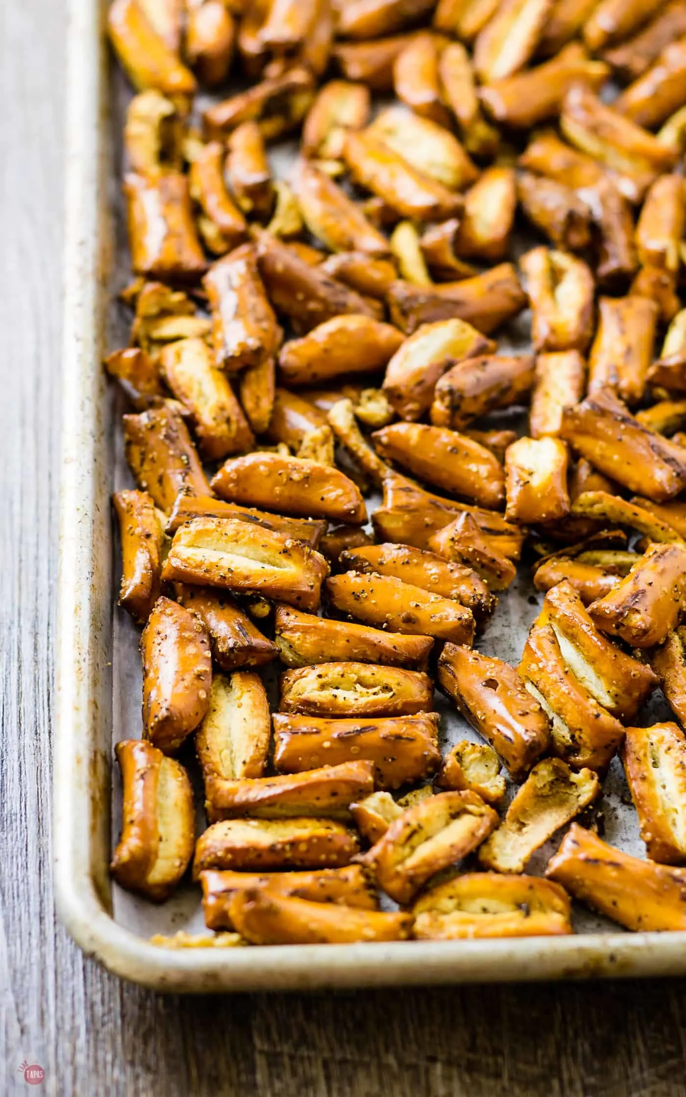 The seasoned pretzels spread out on a sheet pan ready to go in the oven