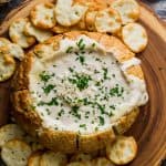 Creamy Beer Cheese Dip in a bread bowl on a serving platter with extra dipping crackers.
